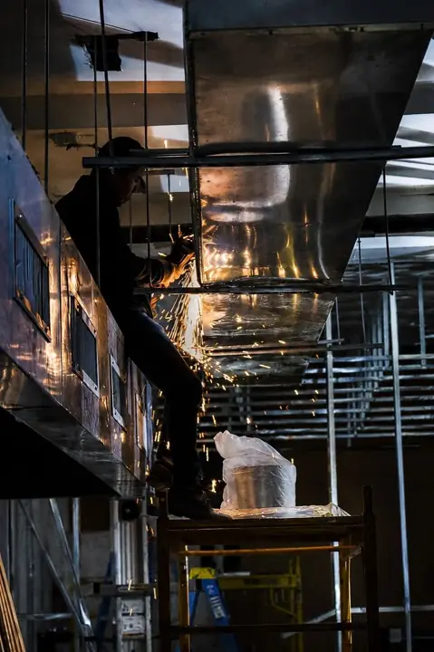 Worker fabricating overhead commercial ductwork